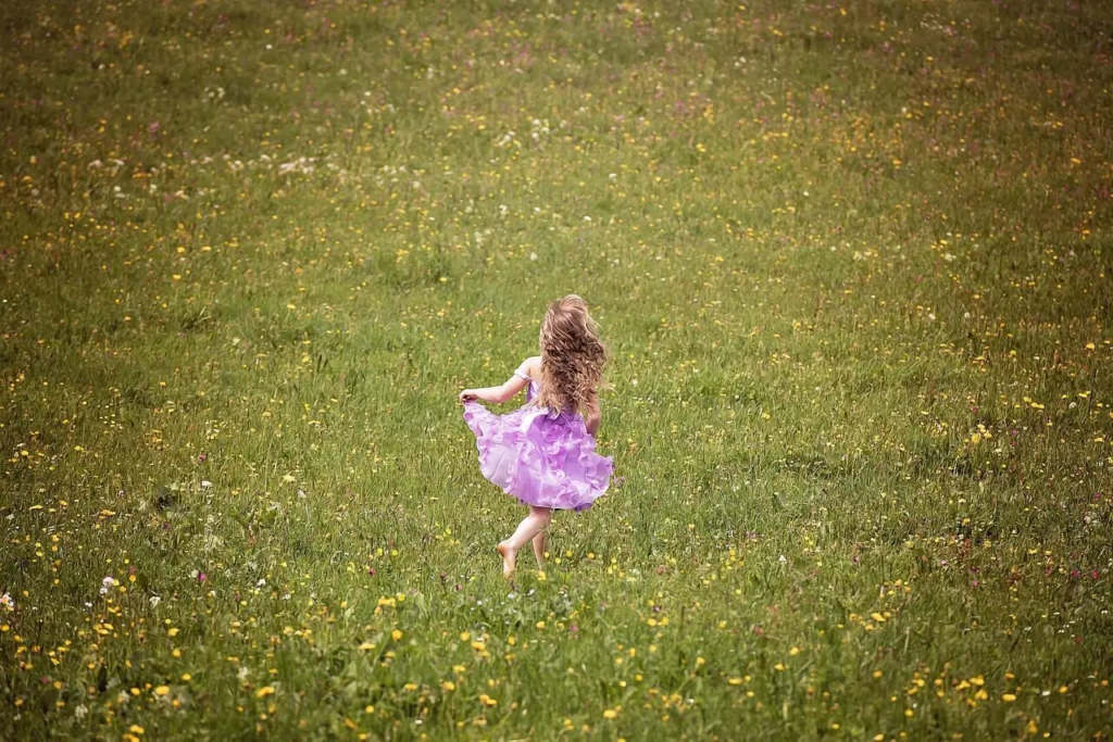 Young girl in a purple dress running joyfully through a field of wildflowers, embracing freedom and innocence