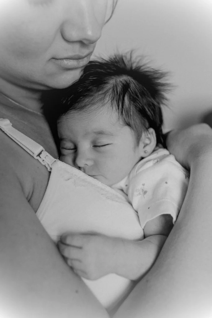 A sleeping newborn cradled gently, soft light on small hands